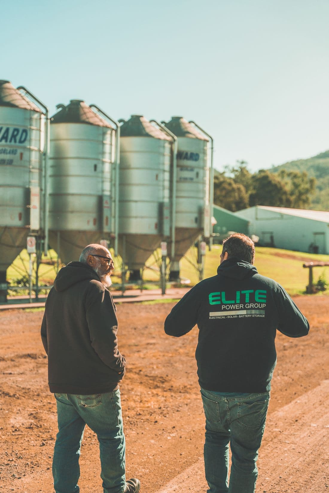 Two people in work clothing talking beside feed silos at a poultry farm